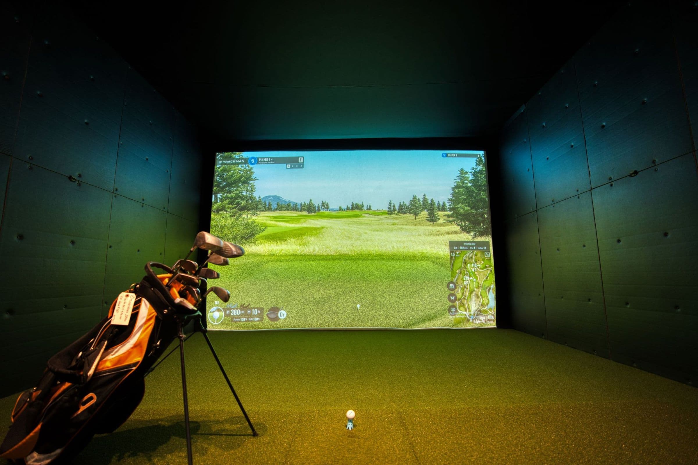 A home golf simulator room at dusk with a projected course on the impact screen